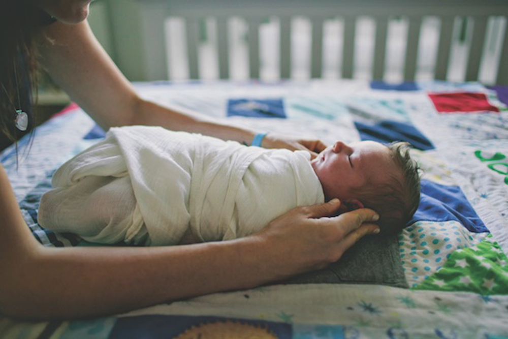 Cropped image of mother touching wrapped baby on bed at home