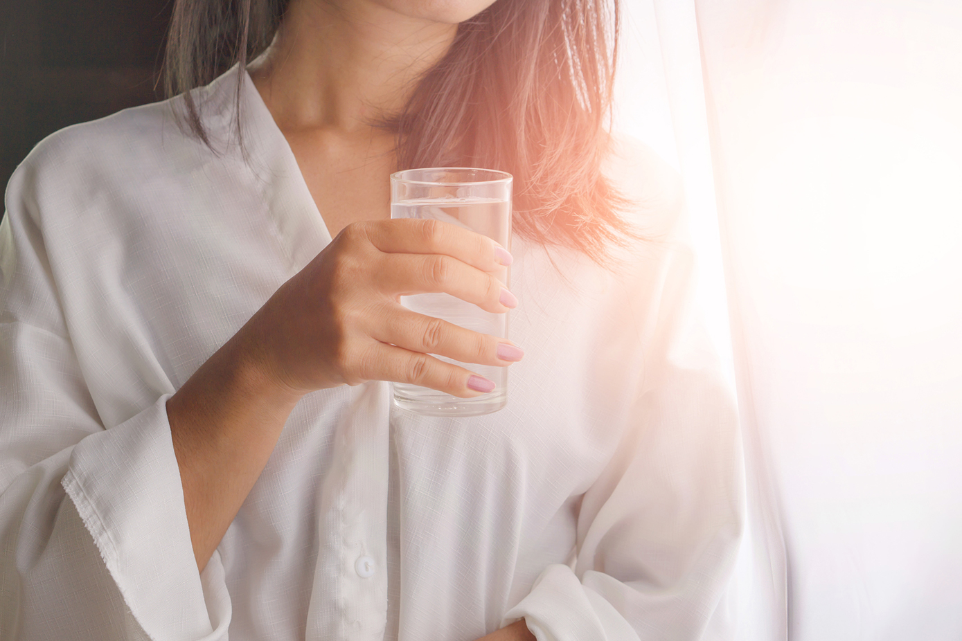 woman drinking water from glass next to the windows